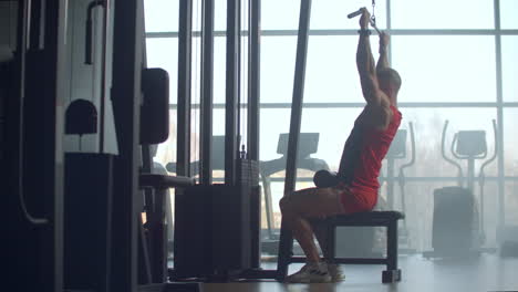 Shoulder-pull-down-machine.-Man-working-out-lat-pulldown-training-at-gym.-Upper-body-strength-exercise-for-the-upper-back.-Fit-male-doing-cross-training-at-gym.-Windows